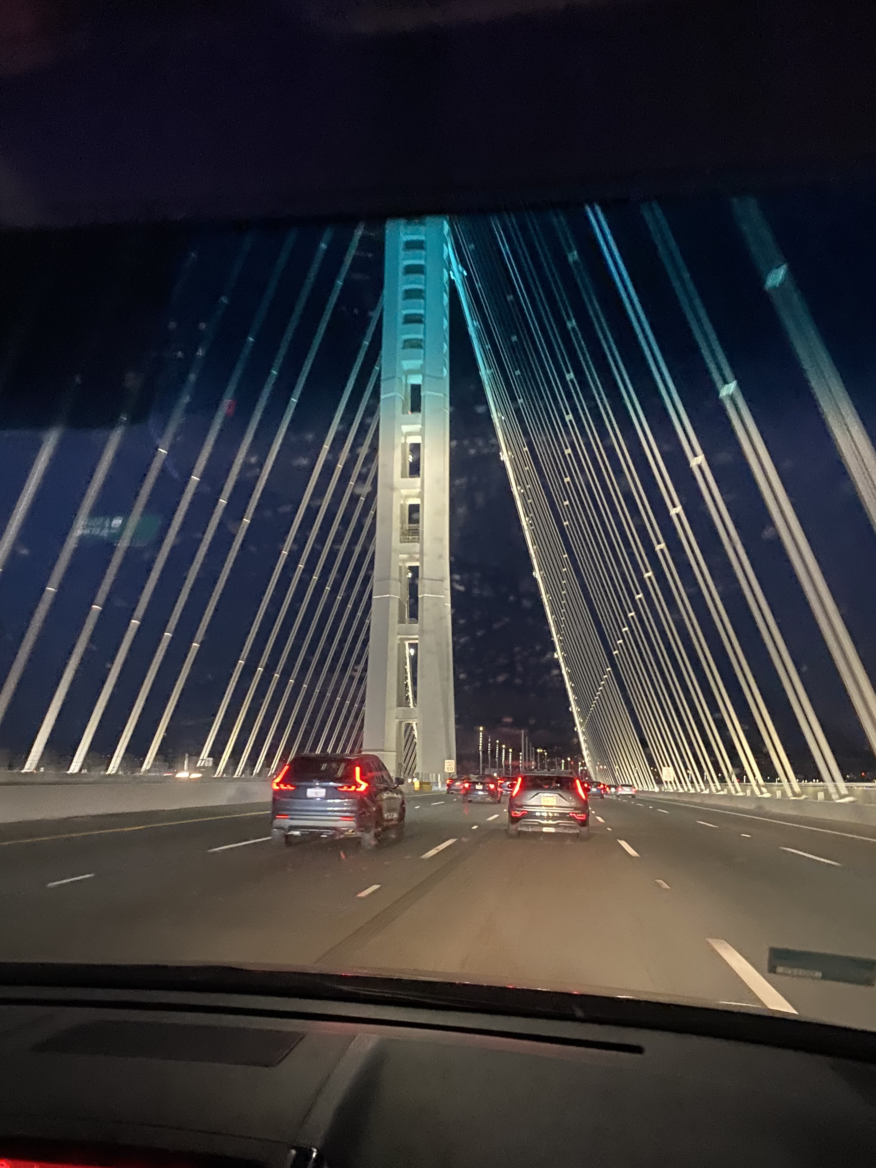 The bay bridge with a dark sky behind, a few cars behind.